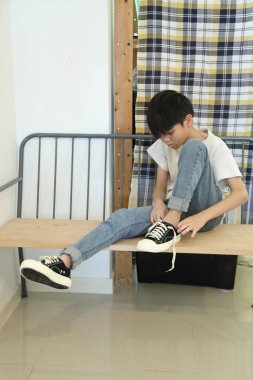 Güneydoğu Asyalı çocuk evden çıkmadan önce ayakkabılarını giyiyor..