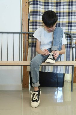 Güneydoğu Asyalı çocuk evden çıkmadan önce ayakkabılarını giyiyor..