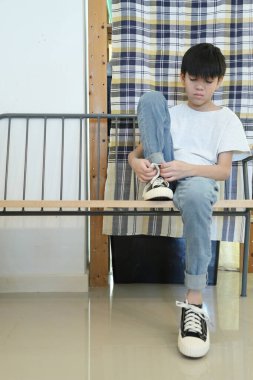 Güneydoğu Asyalı çocuk evden çıkmadan önce ayakkabılarını giyiyor..