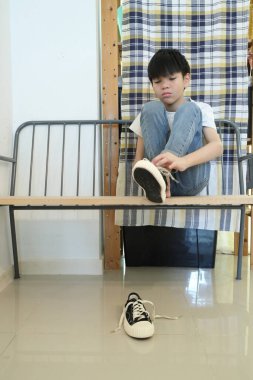 Güneydoğu Asyalı çocuk evden çıkmadan önce ayakkabılarını giyiyor..