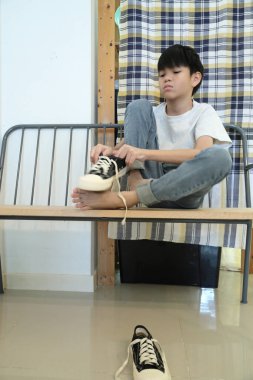 Güneydoğu Asyalı çocuk evden çıkmadan önce ayakkabılarını giyiyor..