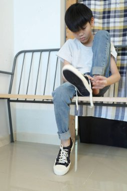 Güneydoğu Asyalı çocuk evden çıkmadan önce ayakkabılarını giyiyor..