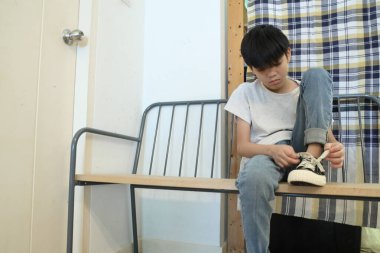 Güneydoğu Asyalı çocuk evden çıkmadan önce ayakkabılarını giyiyor..