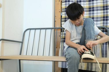 Güneydoğu Asyalı çocuk evden çıkmadan önce ayakkabılarını giyiyor..