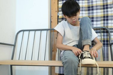 Güneydoğu Asyalı çocuk evden çıkmadan önce ayakkabılarını giyiyor..