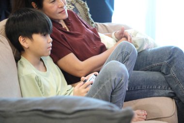 Güneydoğu Asya 'lı bekar anne, genç oğlunun televizyonda oyun oynamasını izliyor..