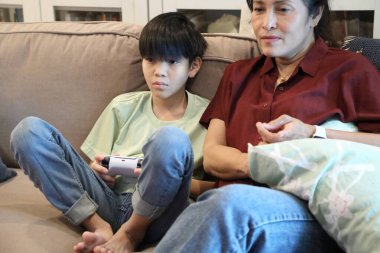 Güneydoğu Asya 'lı bekar anne, genç oğlunun televizyonda oyun oynamasını izliyor..