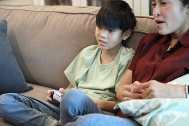 Güneydoğu Asya 'lı bekar anne, genç oğlunun televizyonda oyun oynamasını izliyor..