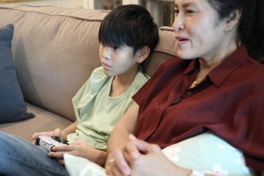 Güneydoğu Asya 'lı bekar anne, genç oğlunun televizyonda oyun oynamasını izliyor..