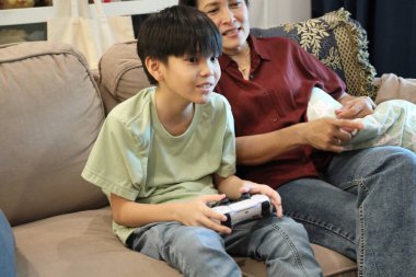 Güneydoğu Asya 'lı bekar anne, genç oğlunun televizyonda oyun oynamasını izliyor..