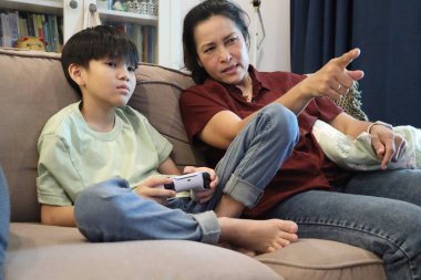 Güneydoğu Asya 'lı bekar anne, genç oğlunun televizyonda oyun oynamasını izliyor..
