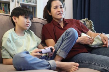 Güneydoğu Asya 'lı bekar anne, genç oğlunun televizyonda oyun oynamasını izliyor..