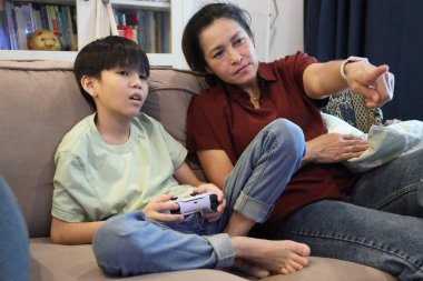 Güneydoğu Asya 'lı bekar anne, genç oğlunun televizyonda oyun oynamasını izliyor..