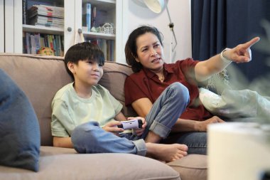 Güneydoğu Asya 'lı bekar anne, genç oğlunun televizyonda oyun oynamasını izliyor..