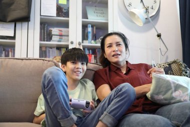 Güneydoğu Asya 'lı bekar anne, genç oğlunun televizyonda oyun oynamasını izliyor..