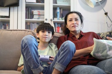 Güneydoğu Asya 'lı bekar anne, genç oğlunun televizyonda oyun oynamasını izliyor..