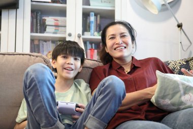 Güneydoğu Asya 'lı bekar anne, genç oğlunun televizyonda oyun oynamasını izliyor..