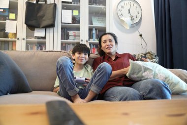 Güneydoğu Asya 'lı bekar anne, genç oğlunun televizyonda oyun oynamasını izliyor..