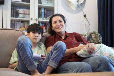 Güneydoğu Asya 'lı bekar anne, genç oğlunun televizyonda oyun oynamasını izliyor..