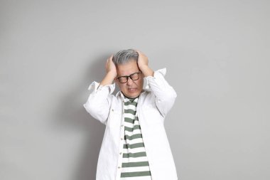 Doğu Asyalı bir adamın portresi gri saçlı ve gözlüklü, şık günlük kıyafetler giymiş, gri bir arka plana karşı duran.