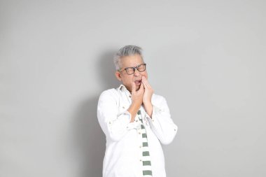 Doğu Asyalı bir adamın portresi gri saçlı ve gözlüklü, şık günlük kıyafetler giymiş, gri bir arka plana karşı duran.