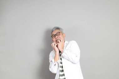 Doğu Asyalı bir adamın portresi gri saçlı ve gözlüklü, şık günlük kıyafetler giymiş, gri bir arka plana karşı duran.