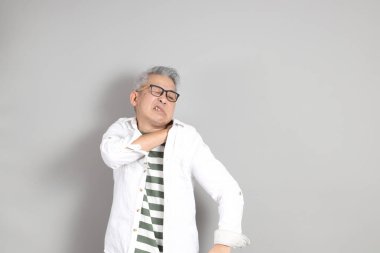 Doğu Asyalı bir adamın portresi gri saçlı ve gözlüklü, şık günlük kıyafetler giymiş, gri bir arka plana karşı duran.