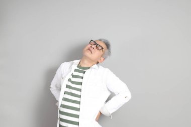 Doğu Asyalı bir adamın portresi gri saçlı ve gözlüklü, şık günlük kıyafetler giymiş, gri bir arka plana karşı duran.