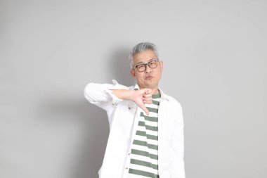 Doğu Asyalı bir adamın portresi gri saçlı ve gözlüklü, şık günlük kıyafetler giymiş, gri bir arka plana karşı duran.