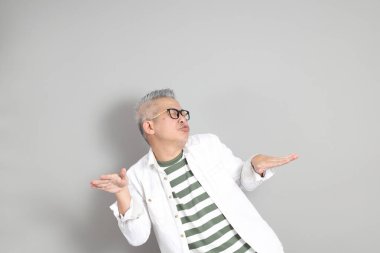 Doğu Asyalı bir adamın portresi gri saçlı ve gözlüklü, şık günlük kıyafetler giymiş, gri bir arka plana karşı duran.