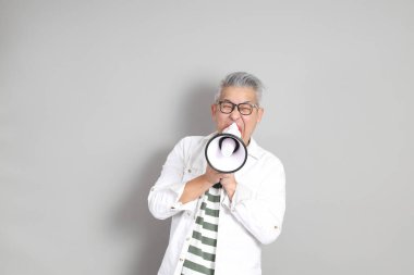 Doğu Asyalı bir adamın portresi gri saçlı ve gözlüklü, şık günlük kıyafetler giymiş, gri bir arka plana karşı duran.