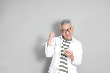 Doğu Asyalı bir adamın portresi gri saçlı ve gözlüklü, şık günlük kıyafetler giymiş, gri bir arka plana karşı duran.