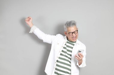 Doğu Asyalı bir adamın portresi gri saçlı ve gözlüklü, şık günlük kıyafetler giymiş, gri bir arka plana karşı duran.