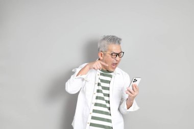 Doğu Asyalı bir adamın portresi gri saçlı ve gözlüklü, şık günlük kıyafetler giymiş, gri bir arka plana karşı duran.