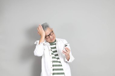 Doğu Asyalı bir adamın portresi gri saçlı ve gözlüklü, şık günlük kıyafetler giymiş, gri bir arka plana karşı duran.