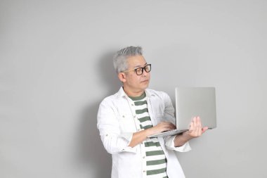 Doğu Asyalı bir adamın portresi gri saçlı ve gözlüklü, şık günlük kıyafetler giymiş, gri bir arka plana karşı duran.