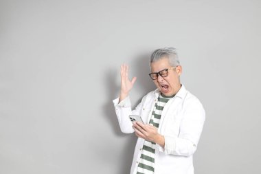 Doğu Asyalı bir adamın portresi gri saçlı ve gözlüklü, şık günlük kıyafetler giymiş, gri bir arka plana karşı duran.