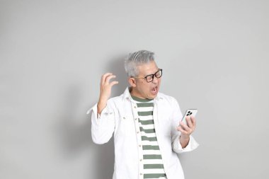 Doğu Asyalı bir adamın portresi gri saçlı ve gözlüklü, şık günlük kıyafetler giymiş, gri bir arka plana karşı duran.