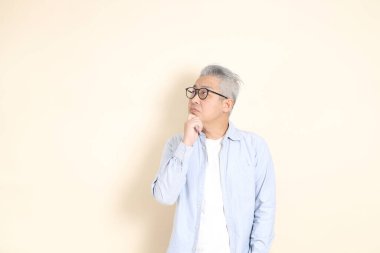 Doğu Asyalı bir adamın portresi gri saçlı ve gözlüklü, şık günlük kıyafetler giymiş, kahverengi arka planda duruyor..