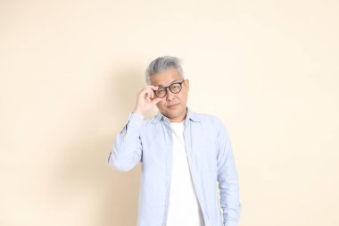 Doğu Asyalı bir adamın portresi gri saçlı ve gözlüklü, şık günlük kıyafetler giymiş, kahverengi arka planda duruyor..