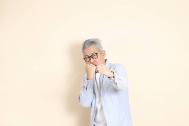 Doğu Asyalı bir adamın portresi gri saçlı ve gözlüklü, şık günlük kıyafetler giymiş, kahverengi arka planda duruyor..