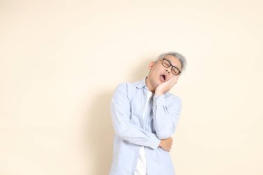 Doğu Asyalı bir adamın portresi gri saçlı ve gözlüklü, şık günlük kıyafetler giymiş, kahverengi arka planda duruyor..