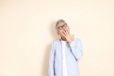 Doğu Asyalı bir adamın portresi gri saçlı ve gözlüklü, şık günlük kıyafetler giymiş, kahverengi arka planda duruyor..