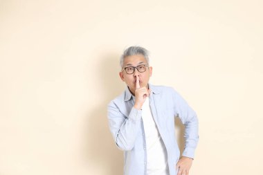 Doğu Asyalı bir adamın portresi gri saçlı ve gözlüklü, şık günlük kıyafetler giymiş, kahverengi arka planda duruyor..