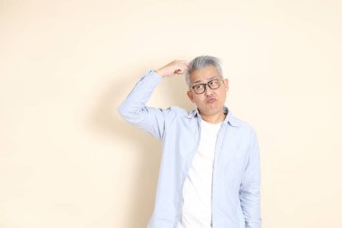 Doğu Asyalı bir adamın portresi gri saçlı ve gözlüklü, şık günlük kıyafetler giymiş, kahverengi arka planda duruyor..