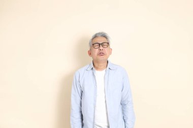 Doğu Asyalı bir adamın portresi gri saçlı ve gözlüklü, şık günlük kıyafetler giymiş, kahverengi arka planda duruyor..