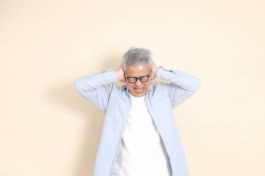 Doğu Asyalı bir adamın portresi gri saçlı ve gözlüklü, şık günlük kıyafetler giymiş, kahverengi arka planda duruyor..