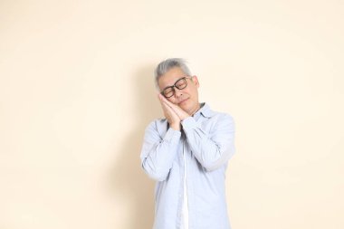 Doğu Asyalı bir adamın portresi gri saçlı ve gözlüklü, şık günlük kıyafetler giymiş, kahverengi arka planda duruyor..