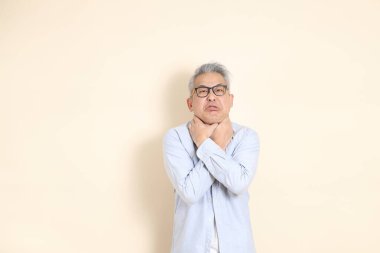 Doğu Asyalı bir adamın portresi gri saçlı ve gözlüklü, şık günlük kıyafetler giymiş, kahverengi arka planda duruyor..