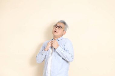 Doğu Asyalı bir adamın portresi gri saçlı ve gözlüklü, şık günlük kıyafetler giymiş, kahverengi arka planda duruyor..